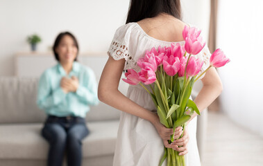 Little Asian girl hiding flowers for her happy grandmother behind back, making holiday surprise at home
