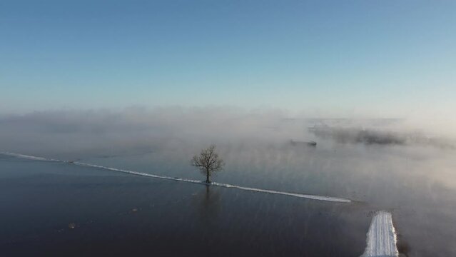 Ship sailing into the fog over the river Ijssel with ice and snow during a cold winter day in The Netherlands. Aerial drone point of view.