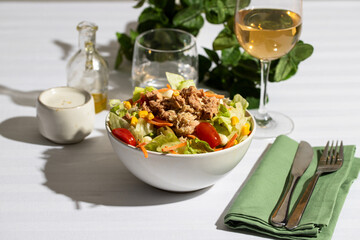 Restaurant table setting with classic tuna salad with  different lettuce, white wine glass, water and cutlery.