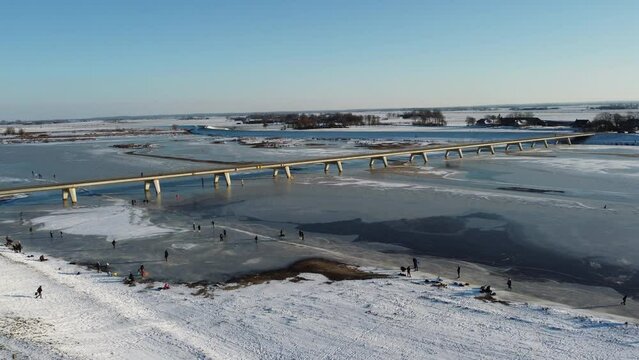 Ice skating people on a frozen lake during a beautiful winter day in The Netherlands. Aerial drone point of view.