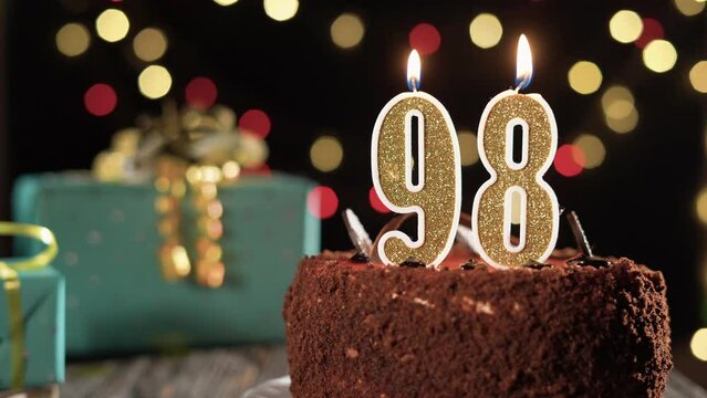 Number ninety-eight birthday candle on a sweet cake on the table, 98th birthday. Fire from the lighter, blow out the holiday candle.