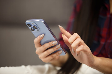 Woman browsing internet on mobile phone. Young adult female with long nails using modern blue smartphone with triple camera