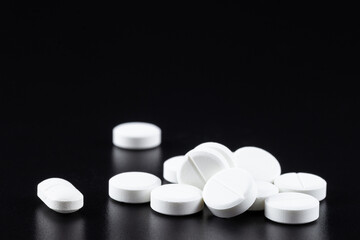 White tablet with two pills in background. Black background with reflection.