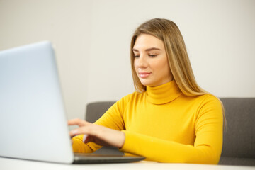 Beautiful blonde woman typing on laptop computer keyboard at home on lockdown. Cheerful entrepreneur person doing distant work online. Young adult female working on modern notebook pc with smile