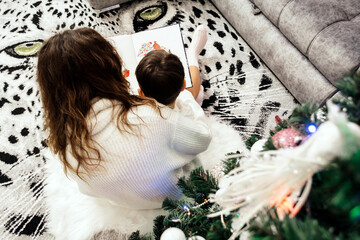 Mom with a child under a Christmas tree with a book