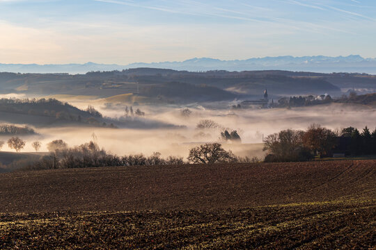 Brume fumante et nappe de nuage au lever du soleil sur le village de Barran dans le Gers et panorama sur les Pyr&eacute;n&eacute;es 