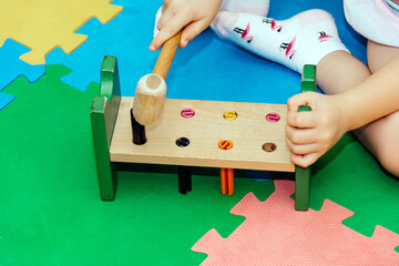 The child plays with a multi-colored children's toy with a wooden mallet