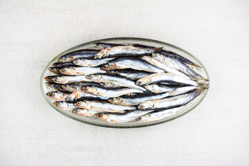 salted fish european anchovy on an oval glass plate on a gray background close-up top view