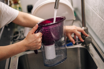 Woman pouring water from faucet into water filter jug at the kitchen. Healthy lifestyle. Woman filling water.