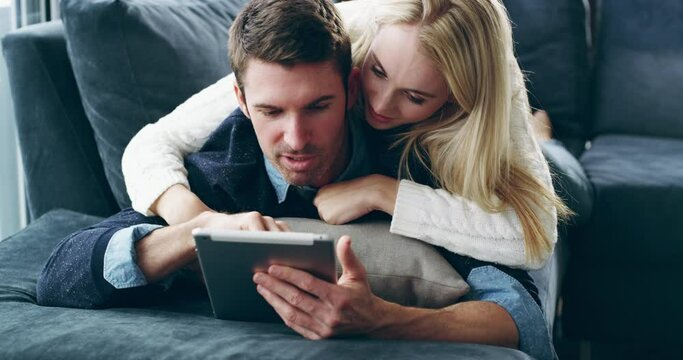 Once again, technology brings people closer. A young happy smiling couple using a digital tablet on the sofa at home. Smiling man and woman relaxing in the lounge together online