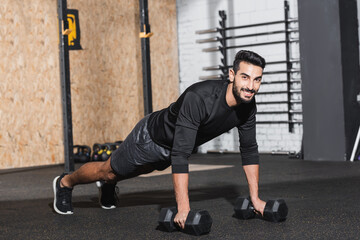 Fototapeta na wymiar Smiling arabian sportsman training with dumbbells in sports center.