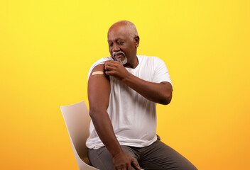Happy elderly black man showing band aid on shoulder after coronavirus vaccination over orange...