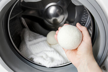 Woman using wool dryer balls for more soft clothes while tumble drying in washing machine concept....