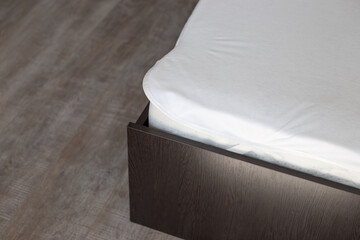 Wooden bed corner with polyurethane mattress and white waterproof cover. Care of bedroom furniture
