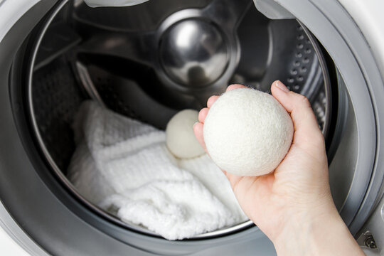 Woman using wool dryer balls for more soft clothes while tumble drying in washing machine concept. Discharge static electricity and shorten drying time, save energy.