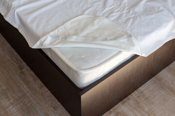 Corner of a wooden bed with a spring mattress and a waterproof mattress topper. Care of home furniture
