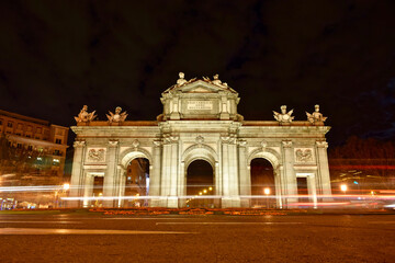 Fototapeta na wymiar Puerta de Alcala at night and full moon. Light trail effect of vehicles passing through the Puerta de Alcala at night with full moon. Front view from the front.