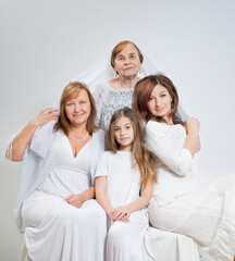 Soft group portrait of women of the same family of different generations in light clothes on a white background.