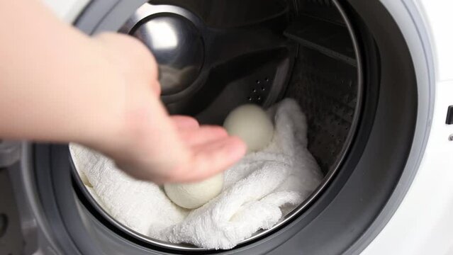 Woman using wool dryer balls for more soft clothes while tumble drying in washing machine concept. Discharge static electricity and shorten drying time, save energy.