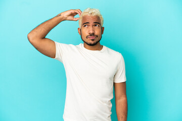 Young Colombian handsome man isolated on blue background having doubts while scratching head