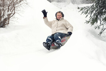 Young at heart concept. Happy smiling elderly mature woman riding on snow tubing. Senior lady sledding slide down hill. Winter fun activity outdoor.