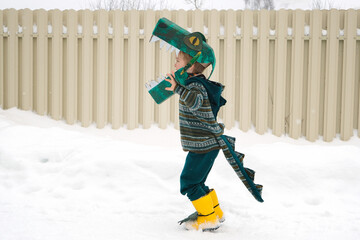 Funny little child in homemade cardboard textile dinosaur or crocodile costume walking on snowy...