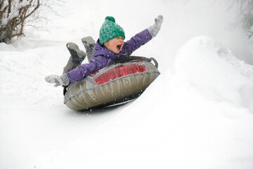 Cute child boy riding on snow tubing rising hands up. Kid sledding slide down hill. Winter fun activity outdoor. - obrazy, fototapety, plakaty