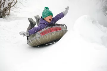 Fotobehang Cute child boy riding on snow tubing rising hands up. Kid sledding slide down hill. Winter fun activity outdoor. © Gargonia