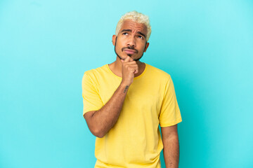 Young Colombian handsome man isolated on blue background having doubts