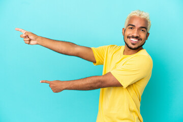 Young Colombian handsome man isolated on blue background pointing finger to the side and presenting a product