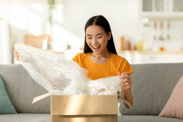 Fast delivery. Happy asian lady received package, unpacking cardboard box, sitting on the sofa at home, copy space - obrazy, fototapety, plakaty