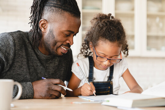 Closeup image of tutoring homeschooling concept. African father dad childminder helping daughter student with homework, drawing together, e-learning, preparing for school art project at home.