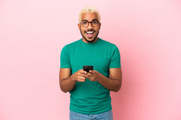Young Colombian handsome man isolated on pink background surprised and sending a message