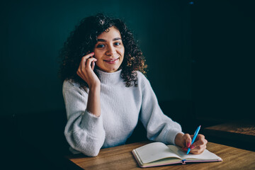 Portrait of happy hipster girl with education textbook for learning or planning organization smiling at camera, carefree woman enjoying time for studying while making mobile conversation for talking