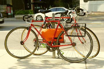 Fototapeta na wymiar Two red locked old road bikes with drop handlebars on circle metal bicycle rack on city street side walk