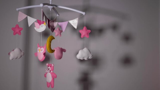 baby mobile with pink hand-stitched animal and bird toys with yellow moon on white wall background. spinning on the baby's crib in the room