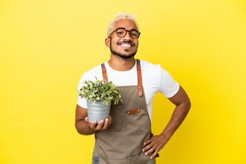 Young Colombian man holding a plant isolated on yellow background posing with arms at hip and...