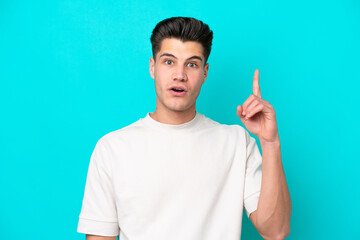 Fototapeta premium Young handsome caucasian man isolated on blue bakcground thinking an idea pointing the finger up
