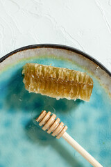 Sealed honeycomb of honey with wooden Honey Dipper for mixing and tasting natural honey on a blue porcelain plate on a white table