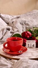 Background Vertical Festive Flatlay, composition for Valentine's Day on February 14. Coffee in a red cup, red rose flowers and diamond heart earrings at home in bed