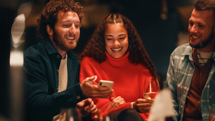 Big Dinner Garden Party Celebration with Happy Friends on a Warm Summer Evening. Charming Man Showing Photos and Videos on His Smartphone. Engaged Men and Female Look at Phone, Talk with Each Other.