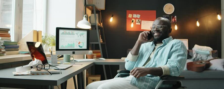 African American businessman with disability sitting in wheelchair and speaking on mobile phone while working at home office