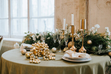 table set for Christmas or New Year's dinner with candles, ornaments, tablecloth and napkins on background of Christmas tree in loft style apartment