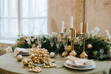 table set for Christmas or New Year's dinner with candles, ornaments, tablecloth and napkins on background of Christmas tree in loft style apartment