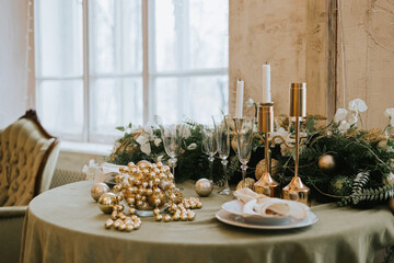 table set for Christmas or New Year's dinner with candles, ornaments, tablecloth and napkins on background of Christmas tree in loft style apartment