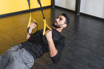 Obraz premium Bearded muslim sportsman training with suspension straps in gym.