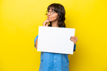 Young nurse doctor woman isolated on yellow background holding an empty placard and thinking