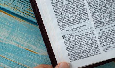 Ten Commandments verse in open Bible Book isolated on blue wooden background with copy space. The biblical concept of wisdom, instruction, and obedience to God Jesus Christ's Holy Law. A closeup.