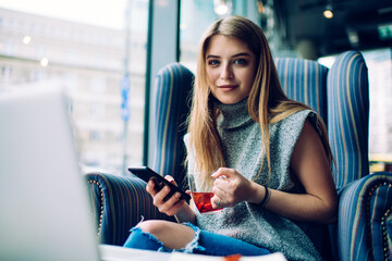 Young charming woman checking messages and drinking tea