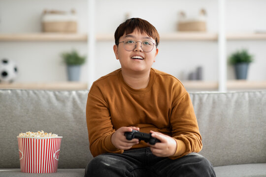 Happy Asian Boy Playing Handheld Video Game At Home